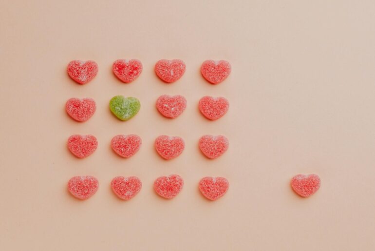 Heart shaped gummy candy assorted in rows with one candy aside against pink background