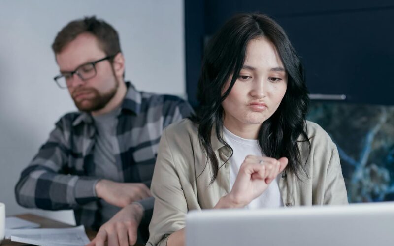 A Man and Woman Sitting at Laptop Frowning