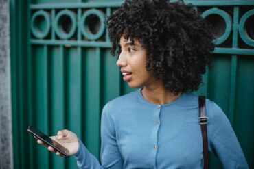 Photo of a Woman in a Blue Top Holding Her Black Smartphone