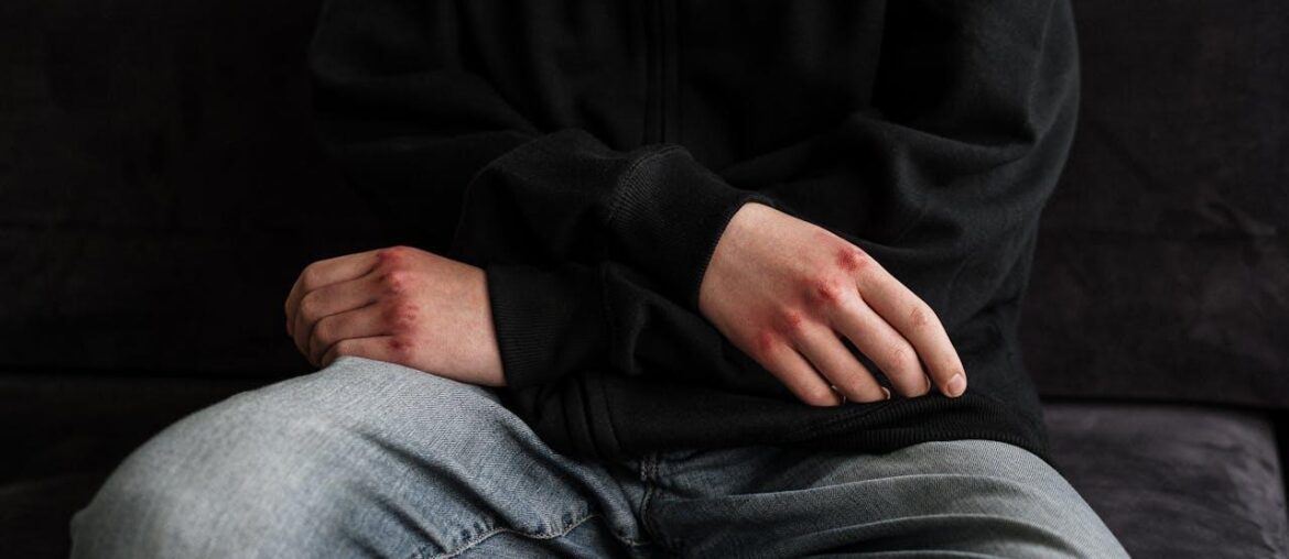 A person in a black jacket and blue denim jeans sitting on a black couch.