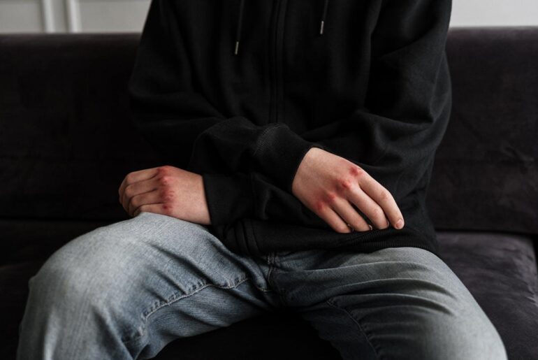 A person in a black jacket and blue denim jeans sitting on a black couch.