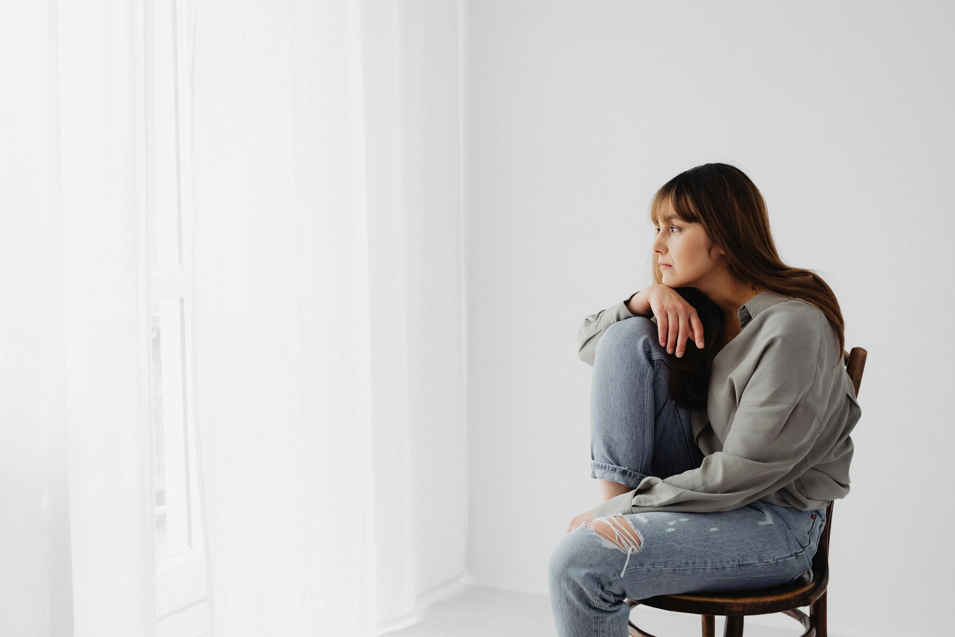 A Woman in Gray Long Sleeves Sitting on Chair Looking Pensive