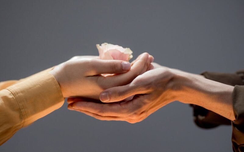 Close-up of Man and Woman Touching Hands and Woman Holding a Rose Flower Head