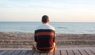 Man Sitting on Wooden Panel Facing in the Ocean