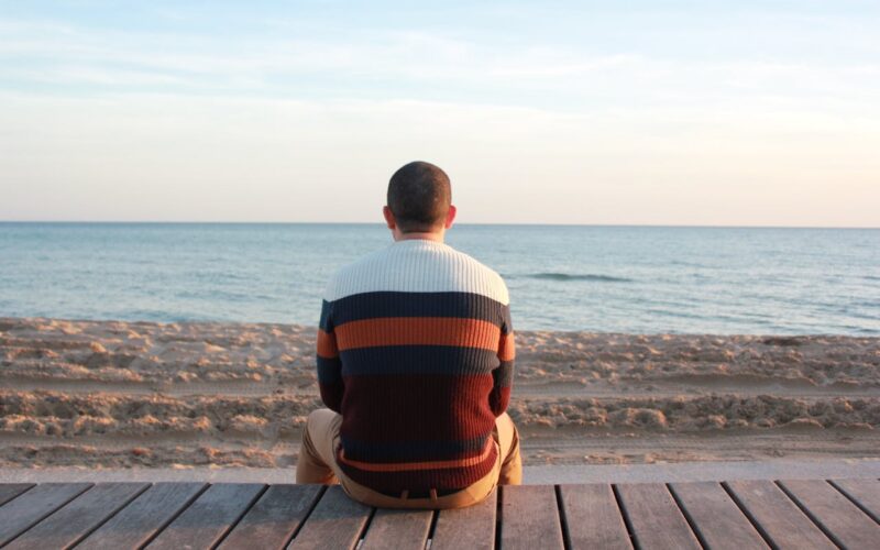 Man Sitting on Wooden Panel Facing in the Ocean