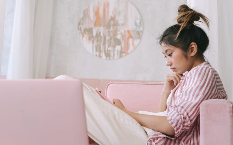 Woman in Pink and White Stripe Shirt Using Her Phone on Sofa