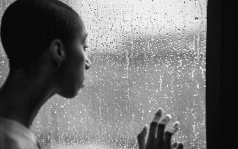 Thoughtful woman standing near window at rainy day