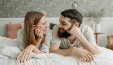 Happy couple lying face to face on a bed, sharing smiles in a cozy and intimate bedroom setting.
