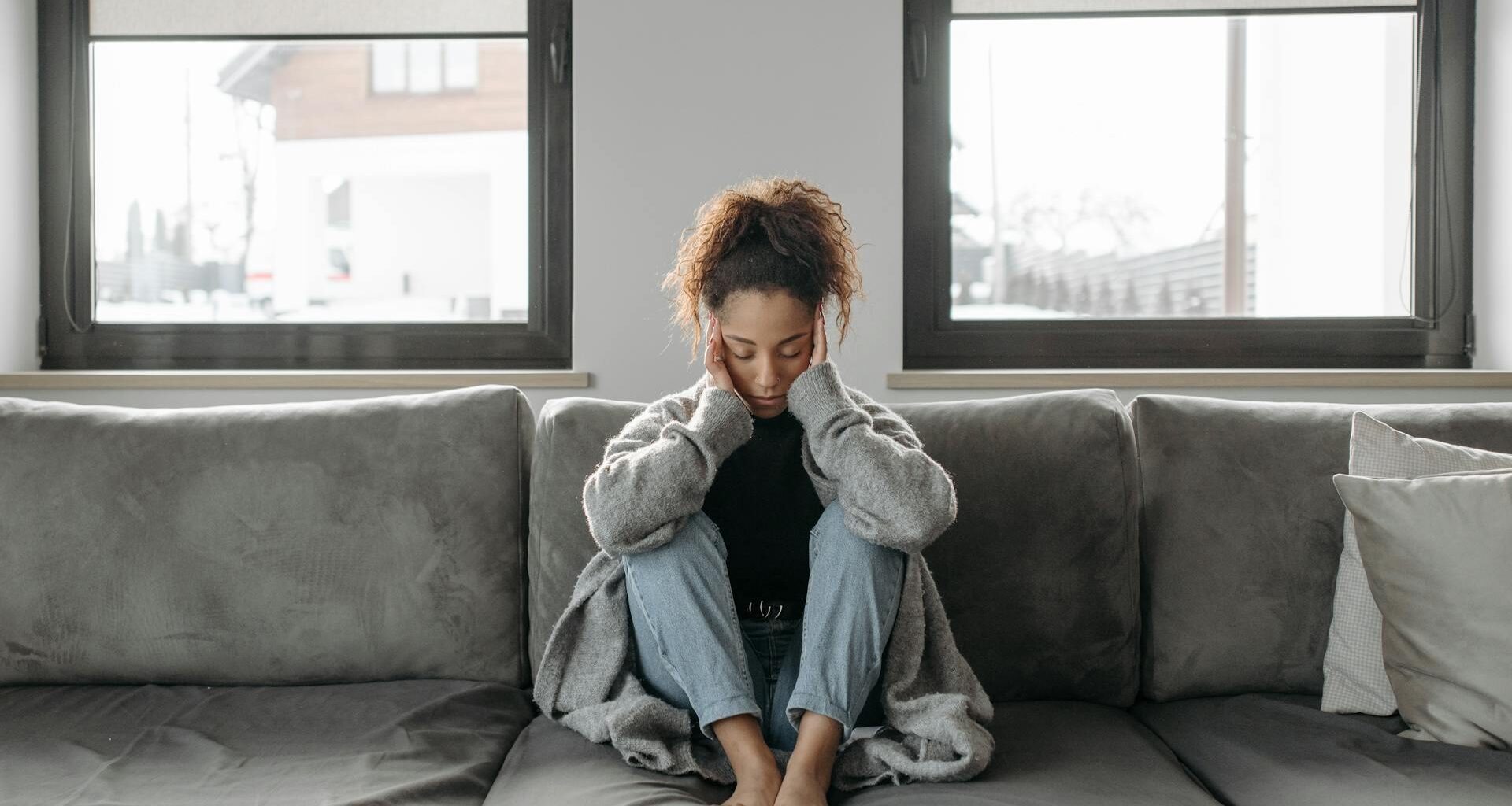 A woman sits on a sofa looking unwell, emphasizing a sense of illness or fatigue indoors