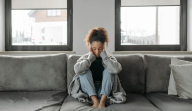 A woman sits on a sofa looking unwell, emphasizing a sense of illness or fatigue indoors