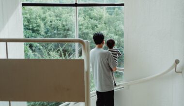 A man holding a child looks out a large window, standing on a staircase.