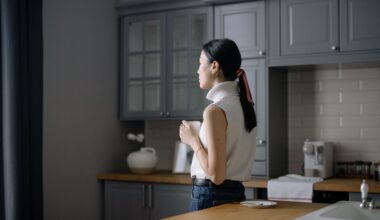 A woman in her kitchen looking away pensively under soft light