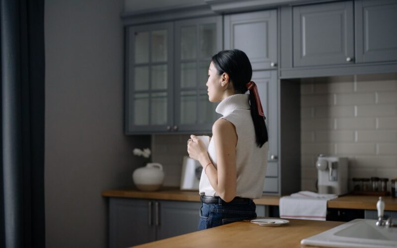 A woman in her kitchen looking away pensively under soft light