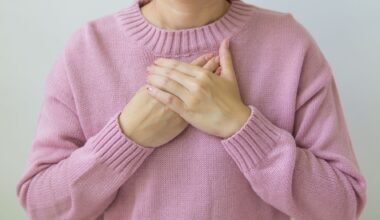 A woman gently places her hands on her chest, wearing a soft pink sweater, symbolizing care and wellness