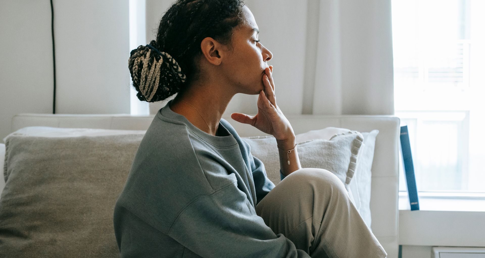 A troubled young woman sits in a relaxed pose in a serene bedroom, reflecting