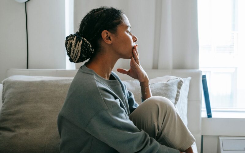 A troubled young woman sits in a relaxed pose in a serene bedroom, reflecting